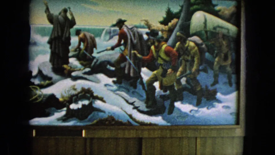 Final frame of the 1964 home-movie clip shows the displayed mural with painted figures in winter clothing, snow-covered terrain, waterfall imagery, and a covered wagon at the right.