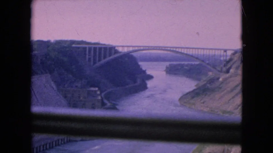 1964 8mm frame showing the same arched bridge and river gorge from a visitor overlook or window-framed vantage point.