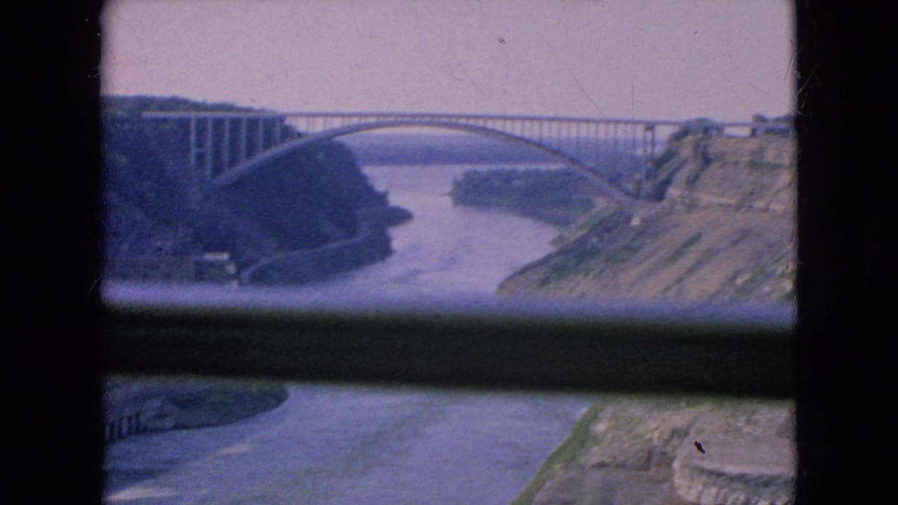 Arched bridge spans a river gorge, partially obscured by dark foreground framing.