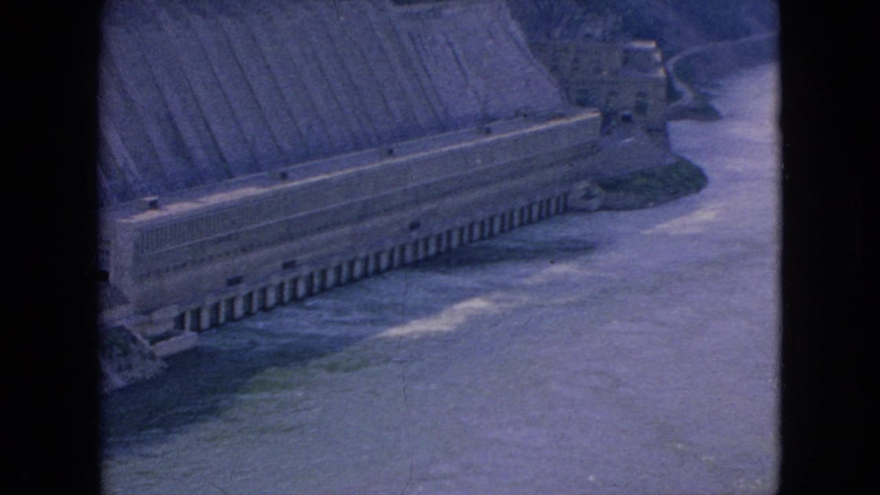 1964 8mm home-movie frame showing an elevated view over a broad river and a long concrete dam structure in the Niagara Falls, New York area.