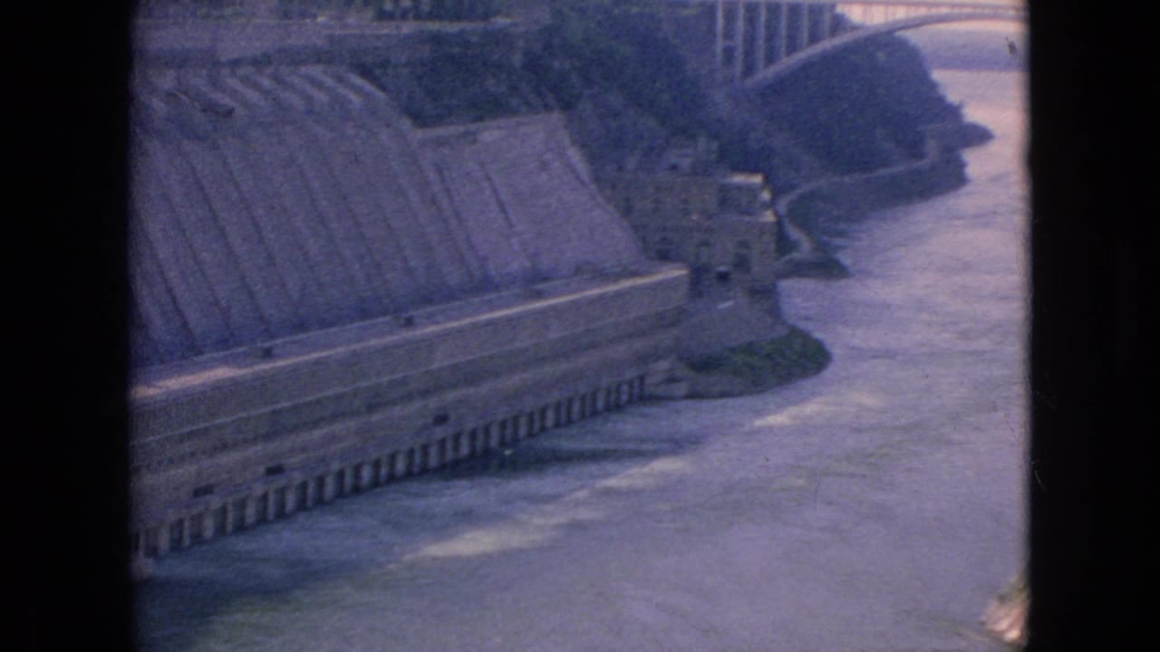 River valley with concrete structure and arched bridge in the distance.
