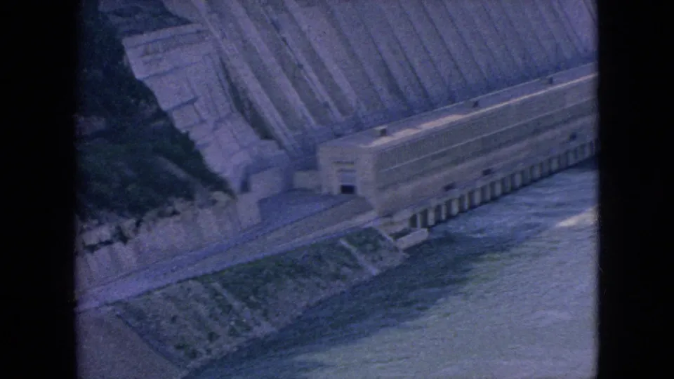 1964 8mm frame showing a large concrete riverbank structure and steep engineered slope beside the Niagara River, seen from an elevated visitor viewpoint.