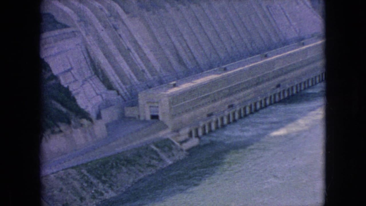 1964 8mm home-movie frame showing a large concrete hydroelectric dam at Niagara Falls, New York, with a stepped spillway and river water below.
