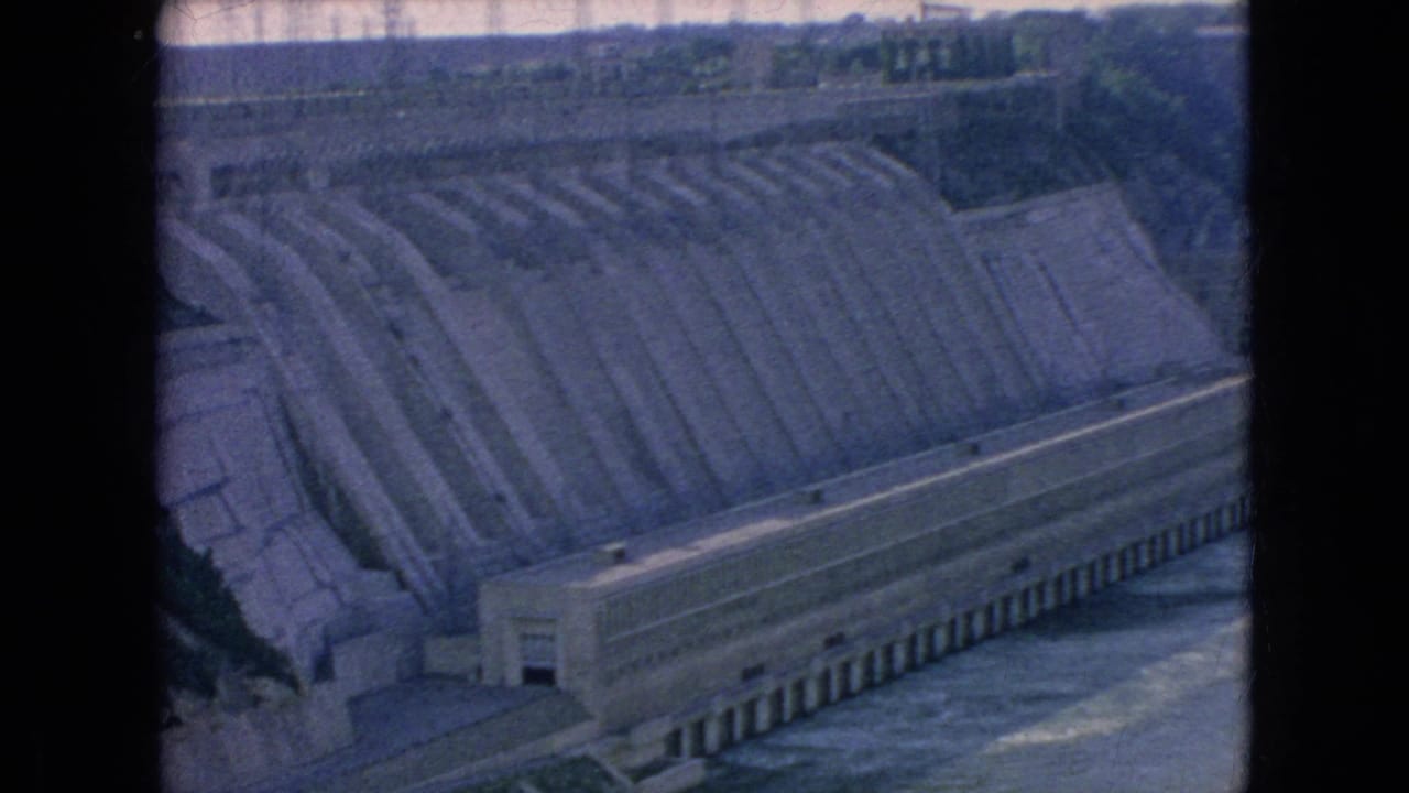 1964 Niagara Falls area 8mm frame showing a stepped concrete spillway above a long base structure with river water below.
