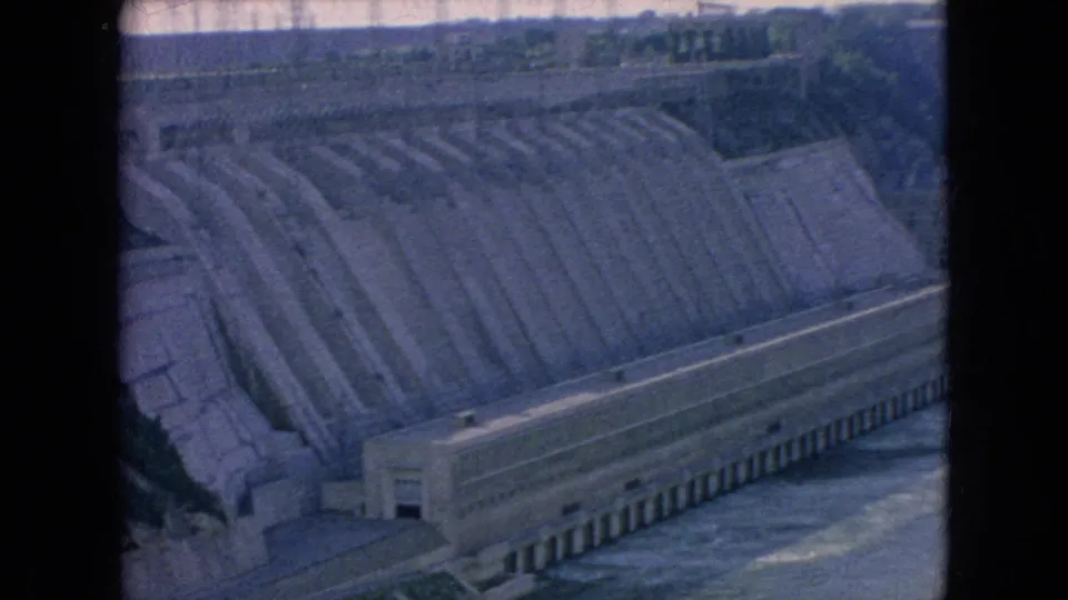 1964 Niagara Falls area 8mm frame showing a stepped concrete spillway above a long base structure with river water below.