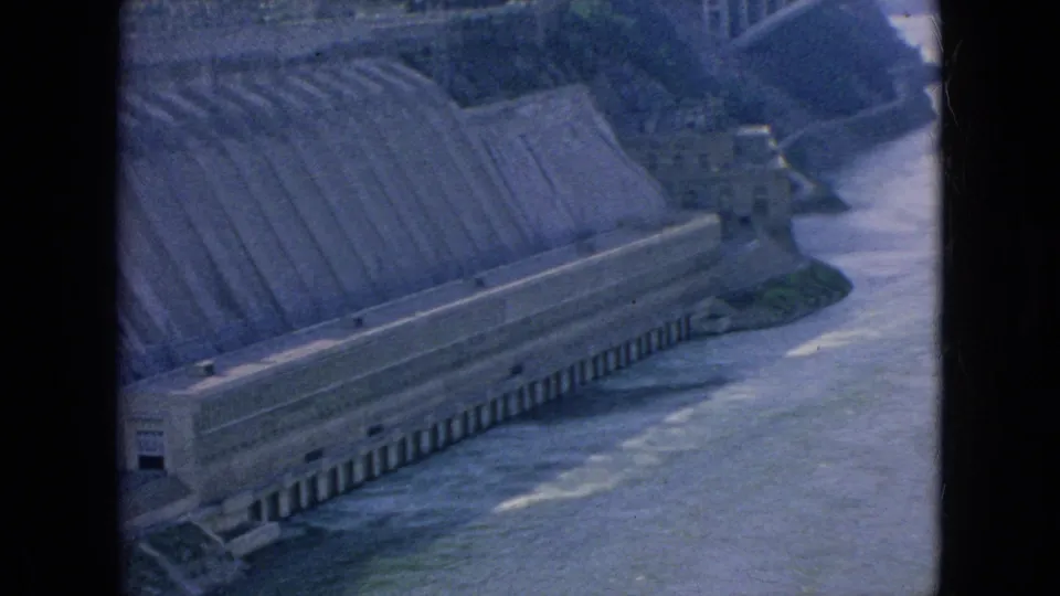 1964 Niagara Falls area 8mm frame showing a tilted visitor view of the spillway wall, long base structure, and moving water below.