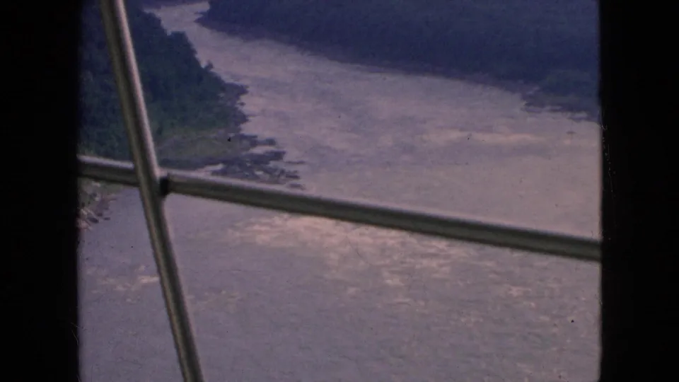 Final 1964 8mm frame looking across the river toward a dark far bank, partially framed by vertical and diagonal bars from the viewing area.