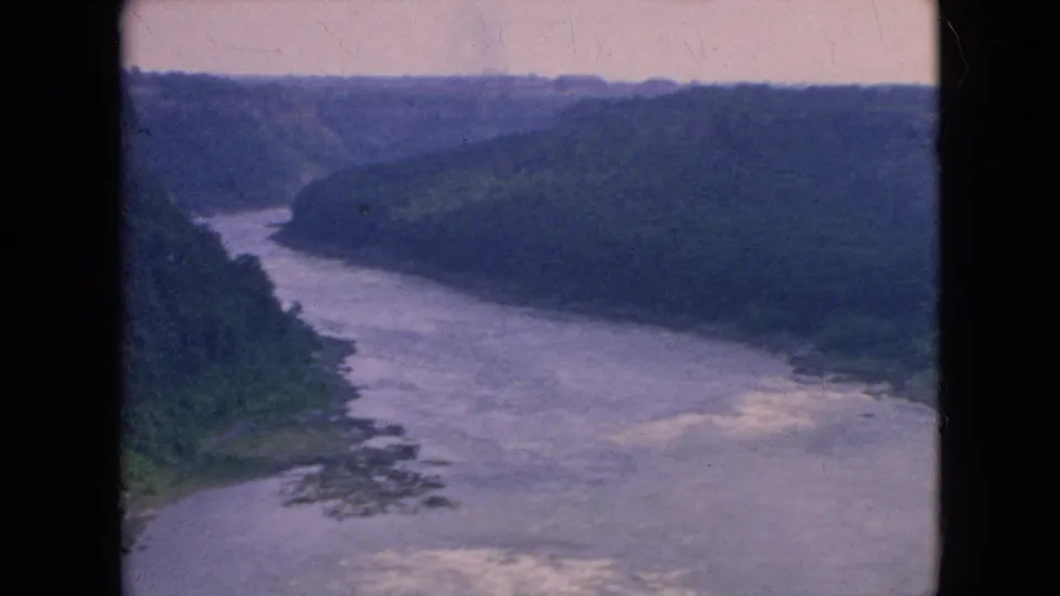 Final frame of the short 8mm clip showing the Niagara Falls area river gorge from above, with pale rapids, wooded slopes, and soft archival color fading.