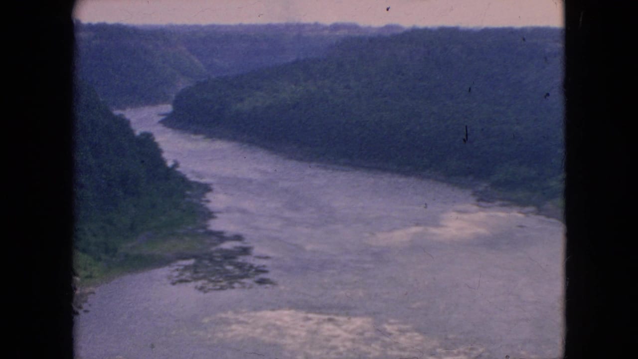 1964 8mm aerial view of a broad white-capped river curving through a forested valley in the Niagara Falls, New York area, framed by dark film borders.