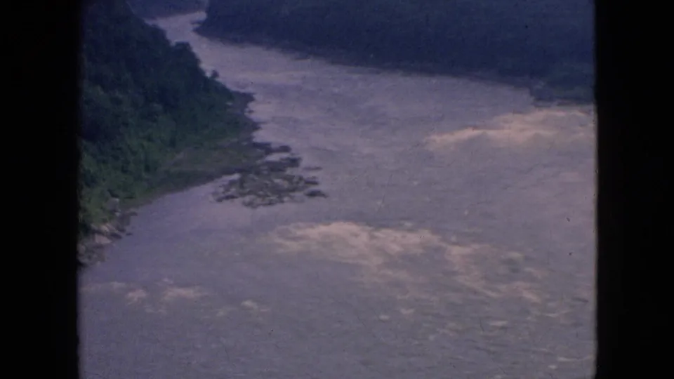 1964 8mm aerial frame of white-capped river water flowing past a wooded shoreline and dark hills in the Niagara Falls, New York area.
