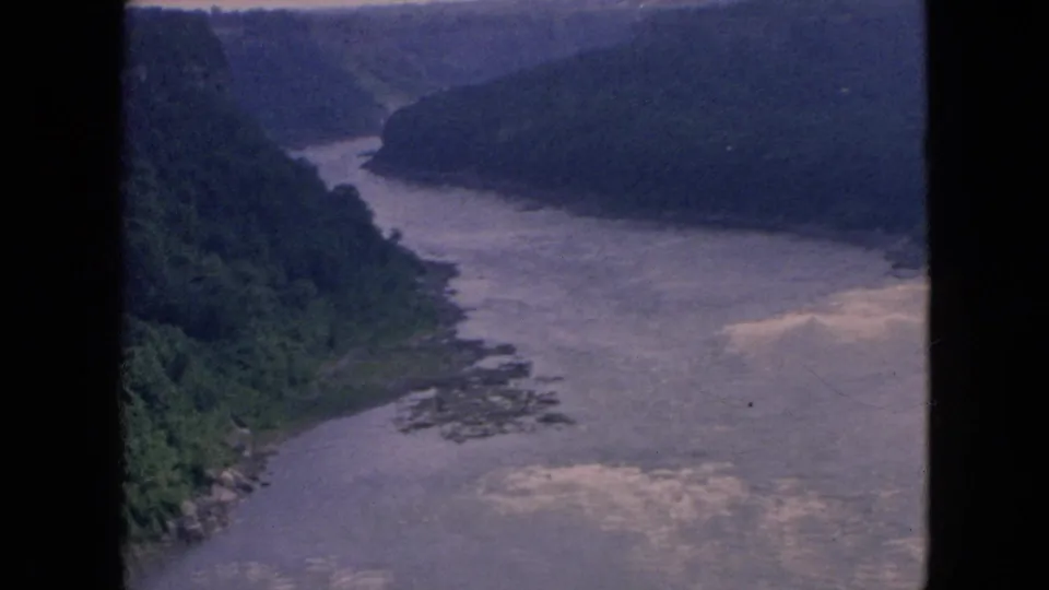 1964 Niagara-area 8mm frame showing the river curving through a wooded gorge, with muted color, soft focus, and bright patches on the water.