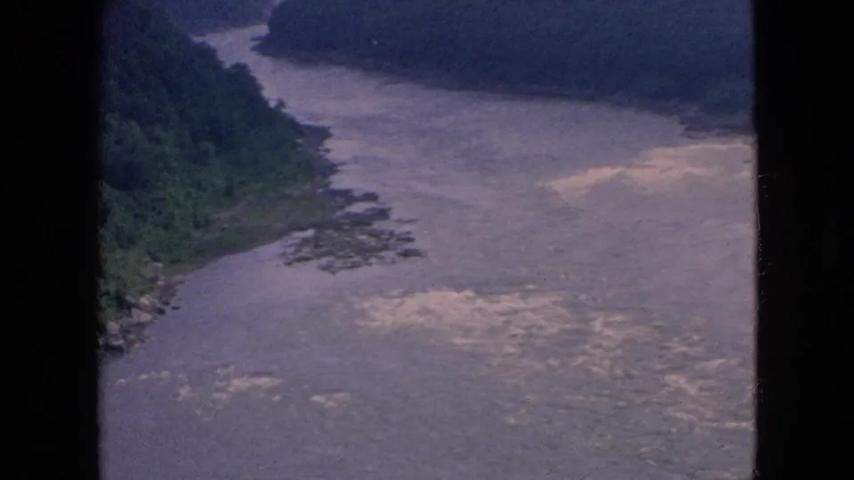 1964 visitor-shot 8mm view across the Niagara River gorge, showing wooded slopes, a wide channel, and bright rippled water near the lower frame.