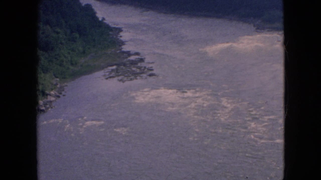 1964 8mm frame associated with Niagara Falls, New York metadata showing a broad water channel with wooded banks and dark film borders.