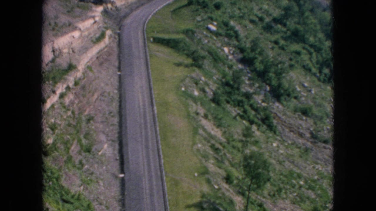 Paved road curving through green slopes and rocky cut terrain.