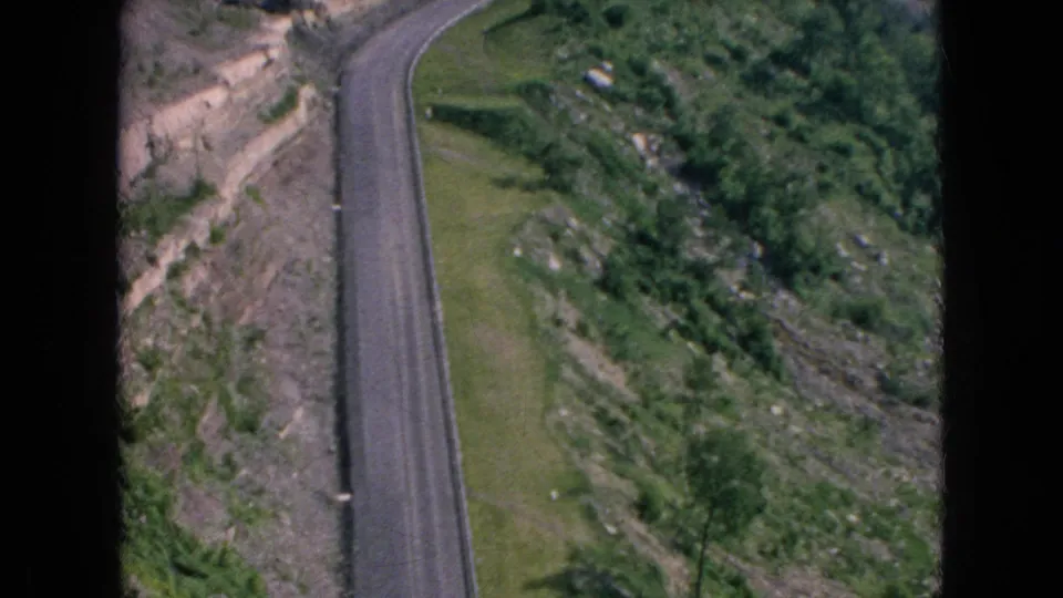 1964 8mm frame associated with Niagara Falls, New York metadata showing a narrow paved road beside exposed rock and green vegetation.