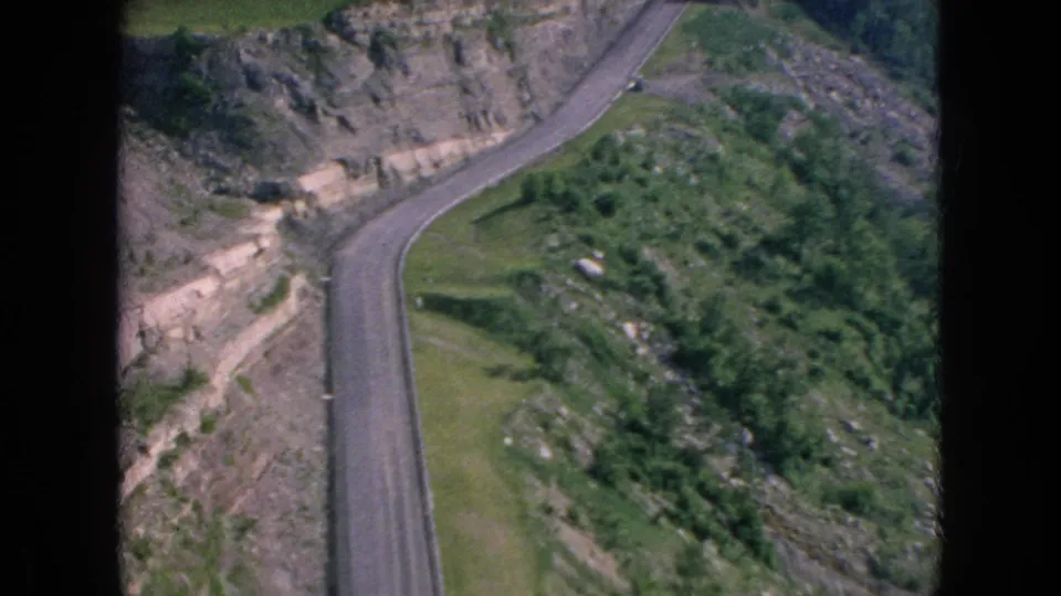 1964 8mm frame associated with Niagara Falls, New York metadata showing a road bending through rocky cut slopes and dense greenery.