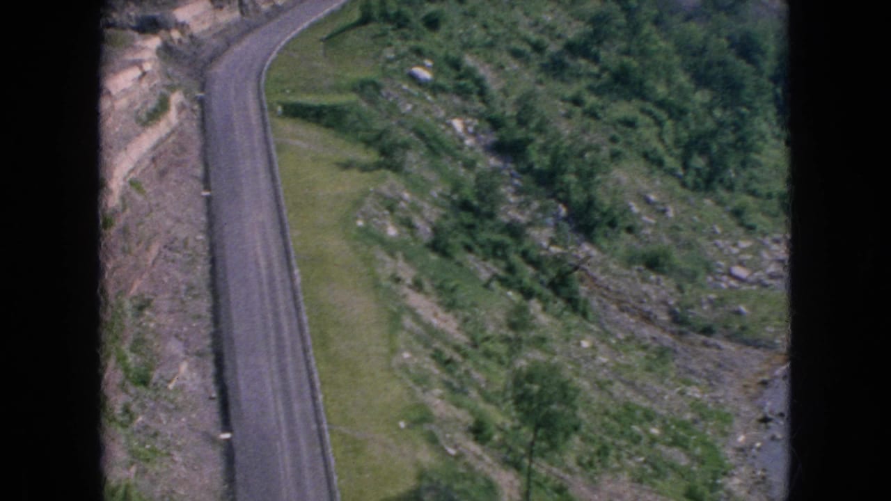 1964 8mm-style high-angle view of a paved road cutting through rocky green hillside terrain in the Niagara Falls, New York travel footage metadata context.