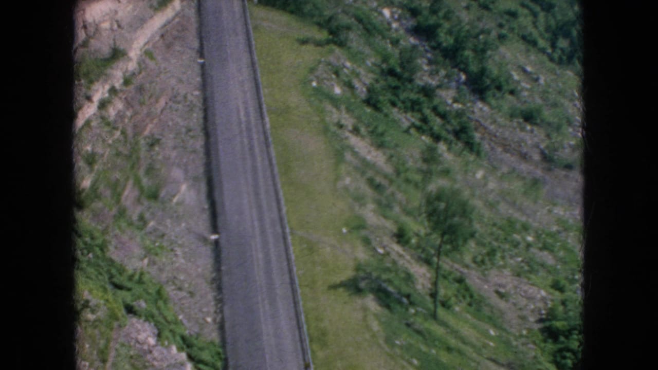 Aerial view of a narrow paved road running beside sloped rocky ground and trees.