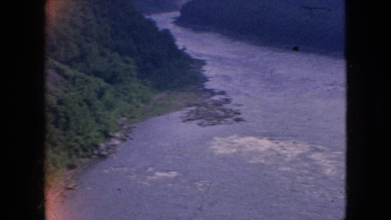 1964 Niagara Falls-area home-movie frame showing a broad river channel bordered by wooded slopes, with soft focus and visible 8mm film edge artifacts.