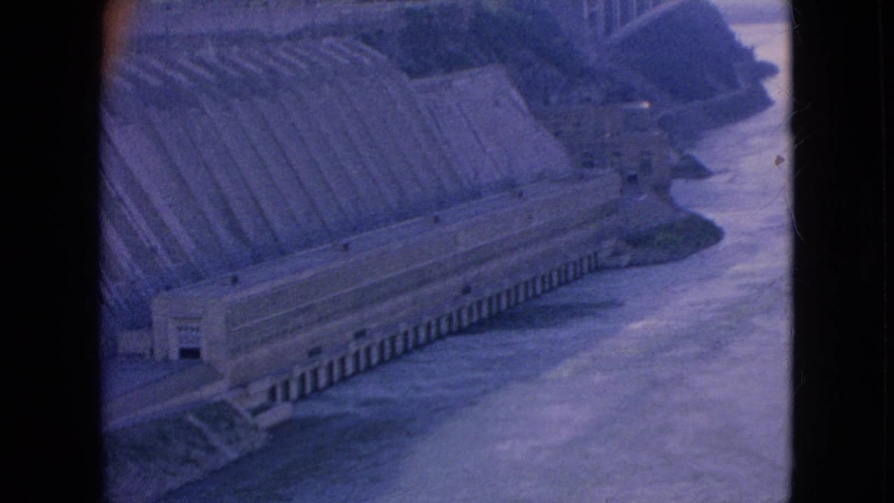 Large concrete dam structure beside a wide river.