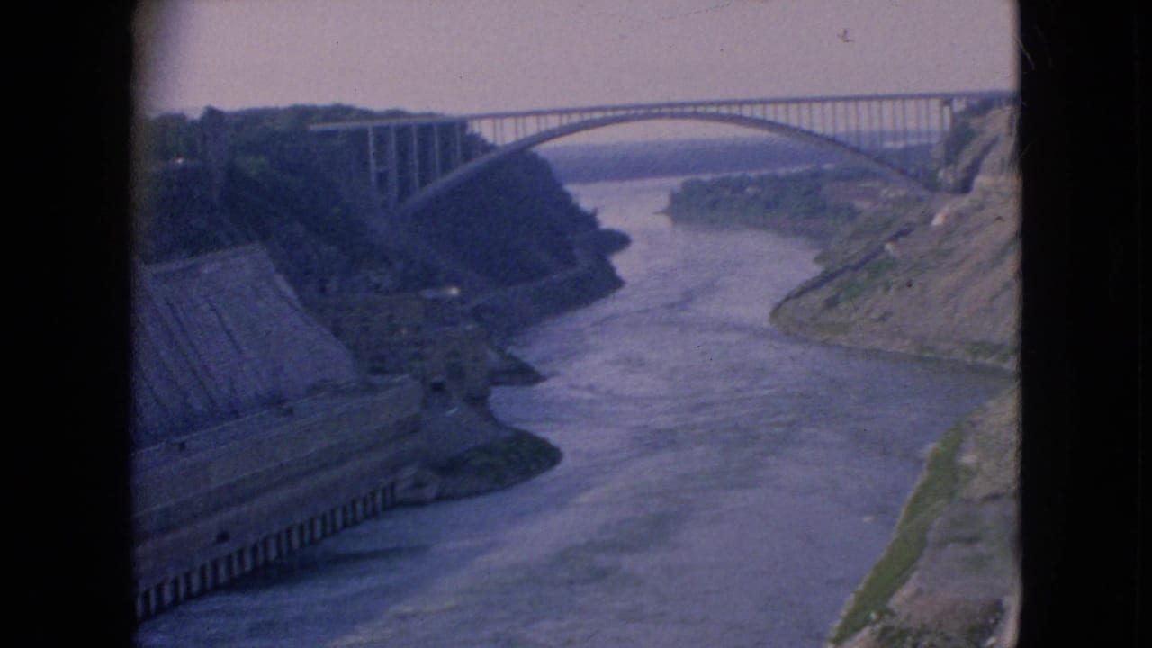 River bends below a high arched bridge between steep cliffs.