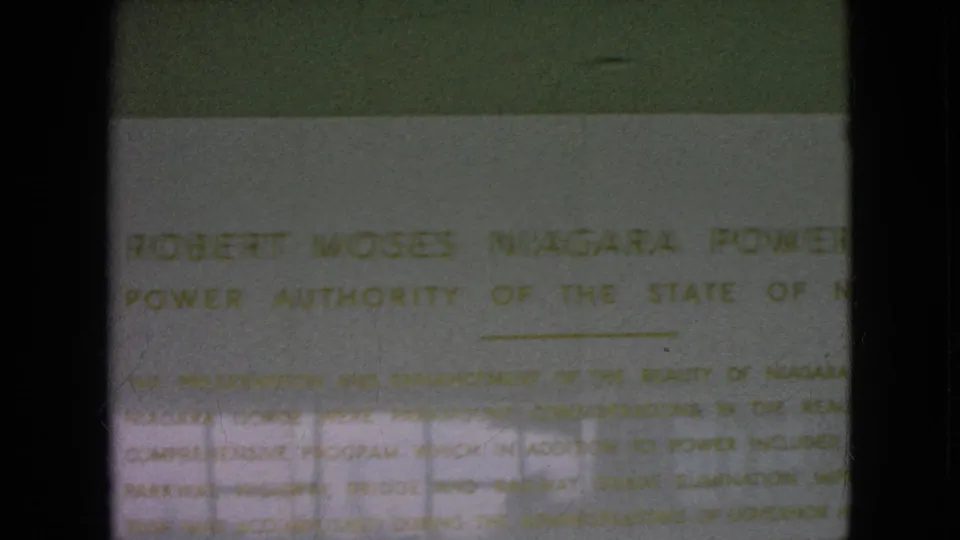 Soft, partially obscured 8mm frame of the Robert Moses Niagara Power Plant plaque with faint official lettering and reflective glare.