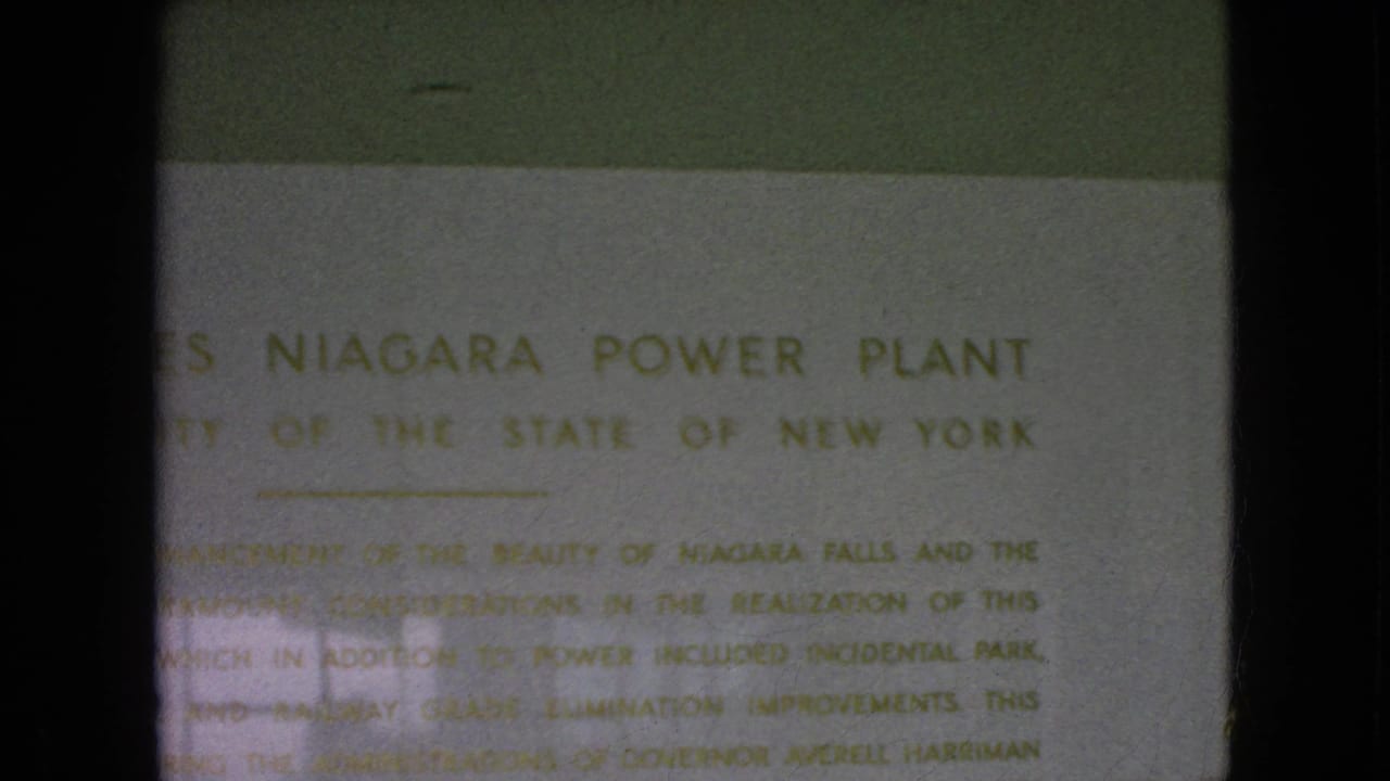 1964 8mm frame showing the Moses Niagara Power Plant sign from a lower handheld position, with explanatory text faintly visible.