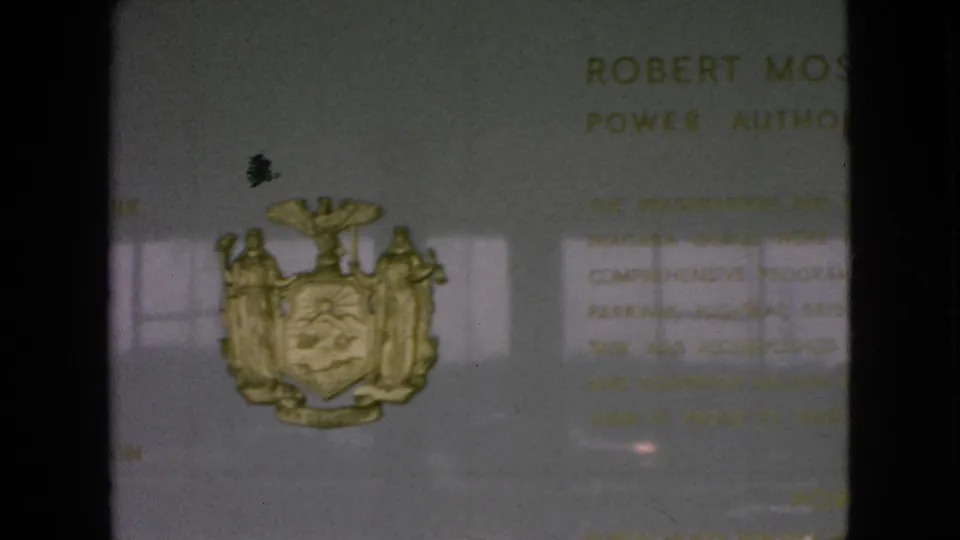 1964 Niagara Falls, New York frame showing a lower view of the commemorative plaque with the gold coat of arms, partial Robert Moses text, and visible film gate shadows.