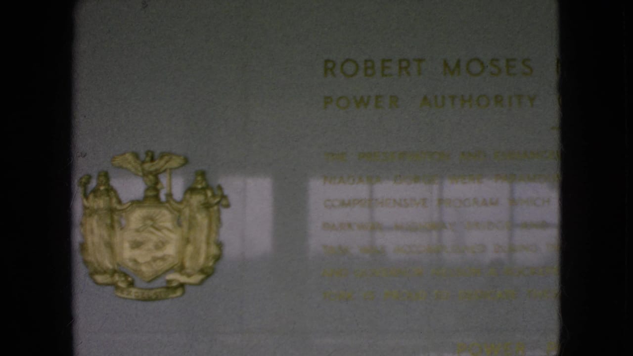 1964 Niagara Falls, New York home-movie frame showing the commemorative plaque with a gold New York State coat of arms and partially readable Robert Moses Power Authority inscription.