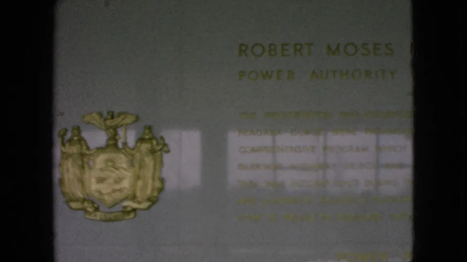 1964 Niagara Falls, New York home-movie frame showing the commemorative plaque with a gold New York State coat of arms and partially readable Robert Moses Power Authority inscription.