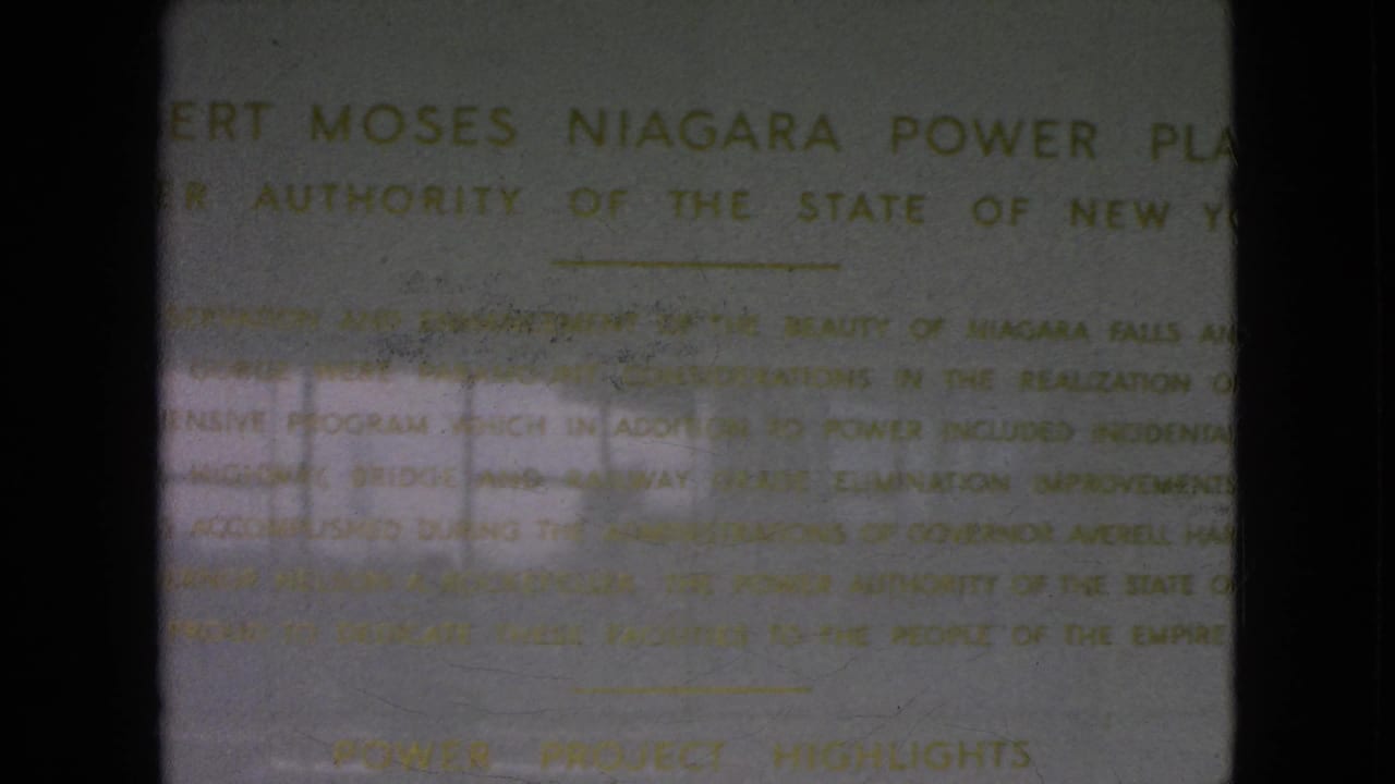 Final 8mm frame showing the Robert Moses Niagara Power Plant heading and inscription text on a pale wall, with dark film borders and uneven reflected light visible in the scan.