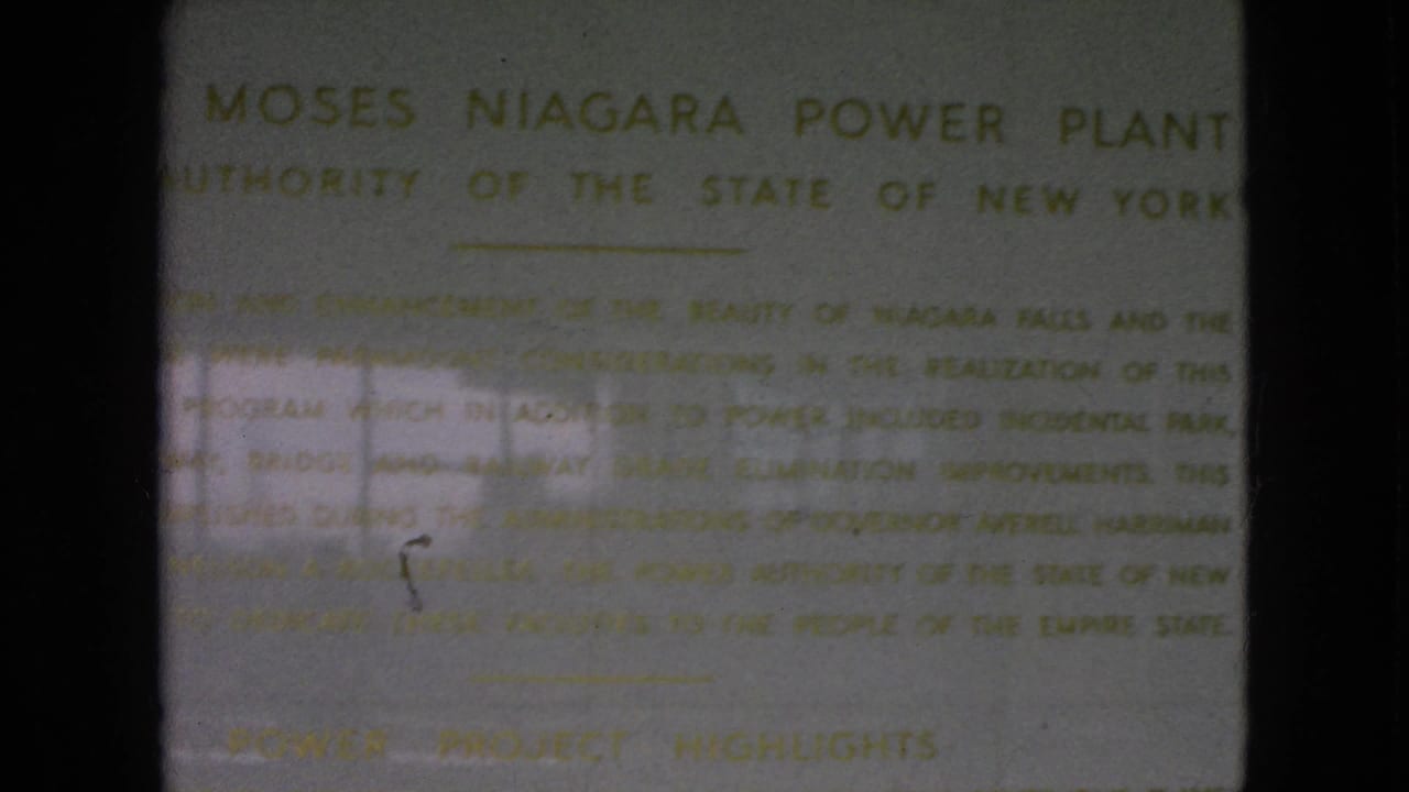 1964 8mm frame showing a close view of the Moses Niagara Power Plant plaque in New York, with soft gold text and dark film borders.