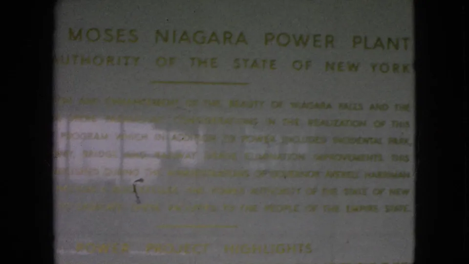 1964 8mm frame showing a close view of the Moses Niagara Power Plant plaque in New York, with soft gold text and dark film borders.