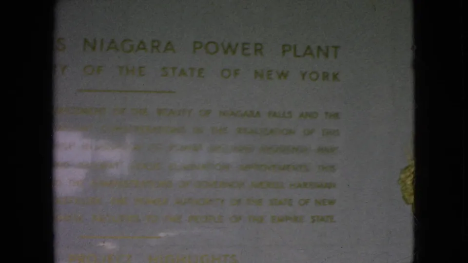 1964 8mm frame of the Moses Niagara Power Plant plaque, showing gold lettering and a partial emblem near the right side of the frame.