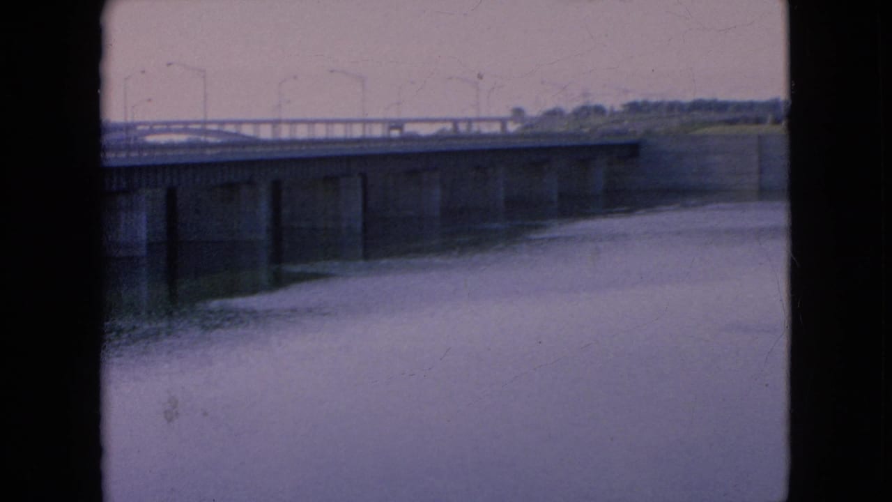 8mm frame from the 1964 Niagara Falls, New York clip showing a low, slightly blurred view of bridge railings, concrete structure, and quiet river water.