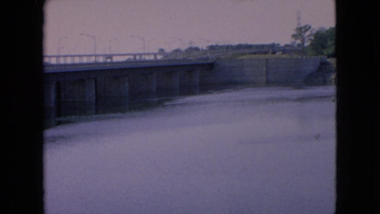 Bridge span and lamp posts above a wide water surface with dark film borders.