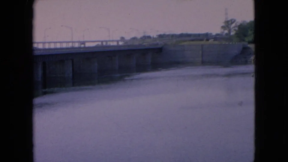 The bridge remains centered over the waterway, with evenly spaced lamp posts along the roadway and a muted purple-blue 8mm color cast.