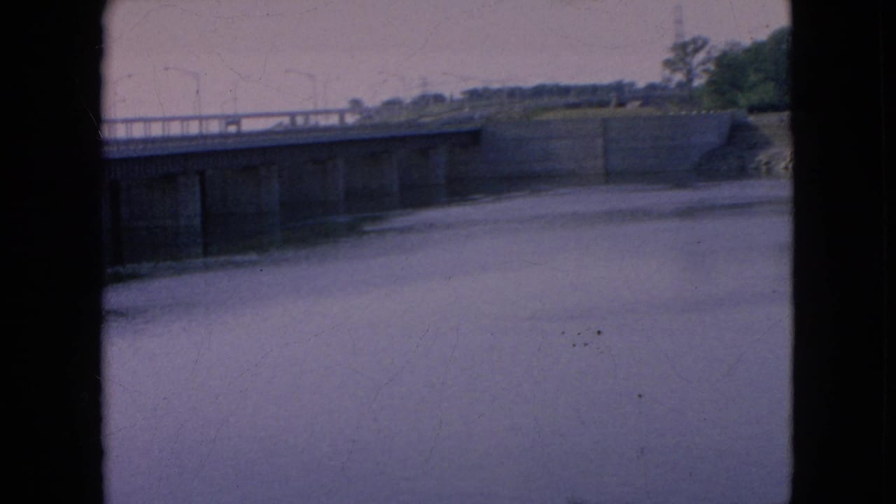 A slightly shifted 8mm frame shows the bridge deck, lamp posts, and calm water below, with the physical film edge prominent at the side.