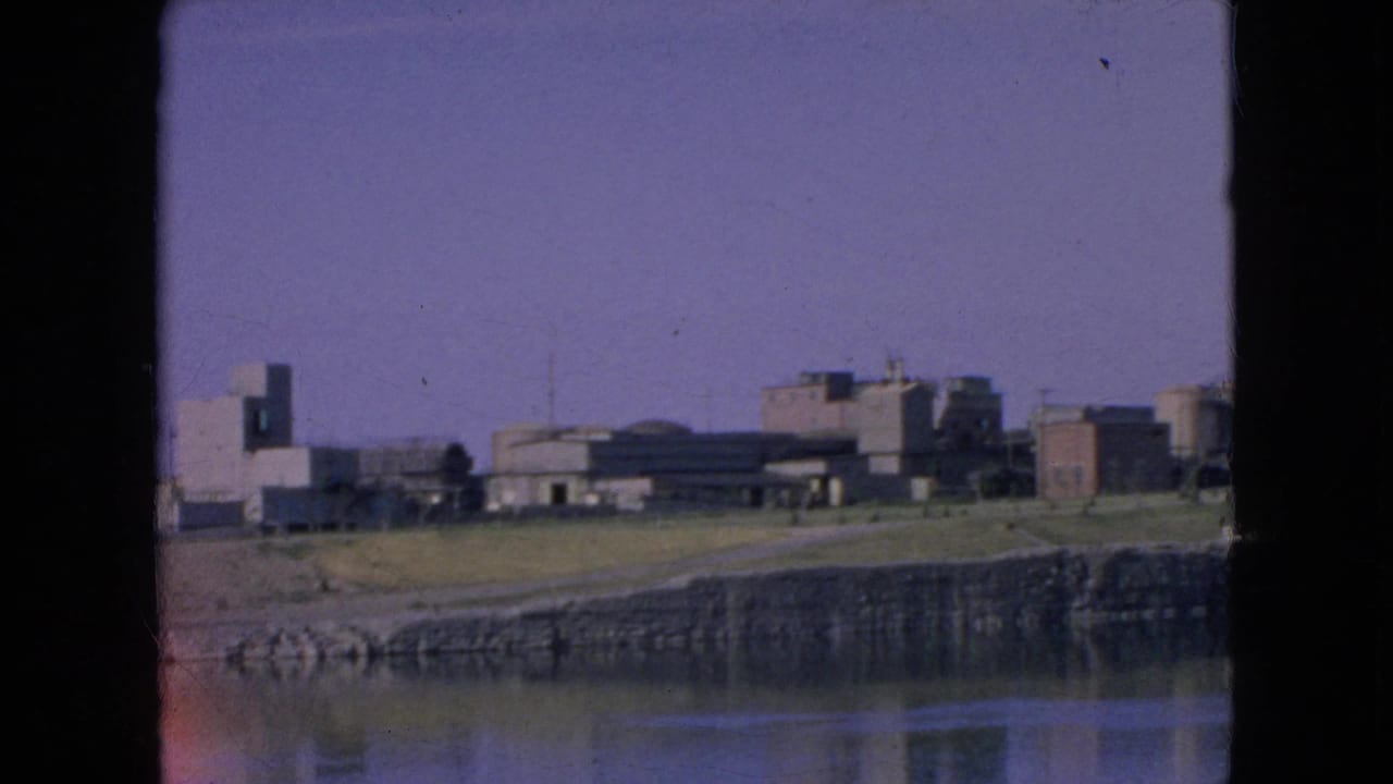 Distant 1964 view of Alcatraz from across San Francisco Bay, with institutional buildings on the island, still water in the foreground, and visible film-frame edges.