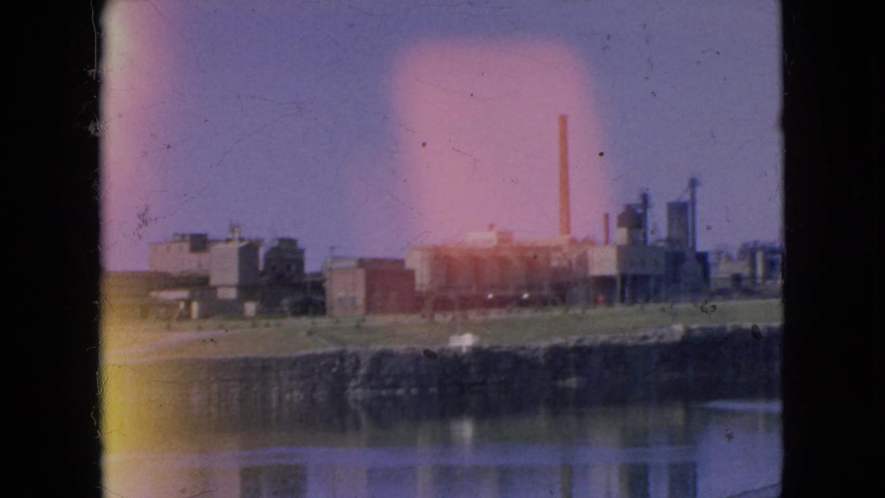 Factory complex across water with strong light leak over the frame.