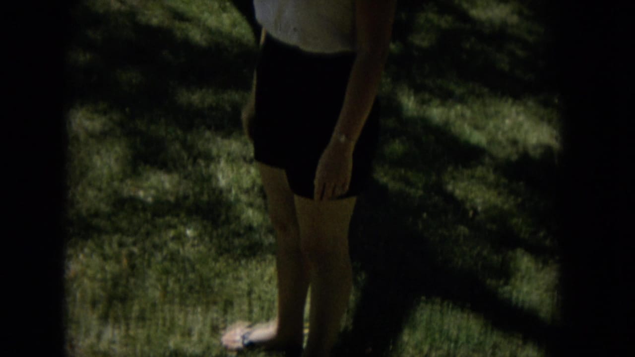 The woman stands in the garden as a dark band obscures part of the contact-sheet frame, leaving her skirt, legs, arm, and shaded lawn clearly visible.