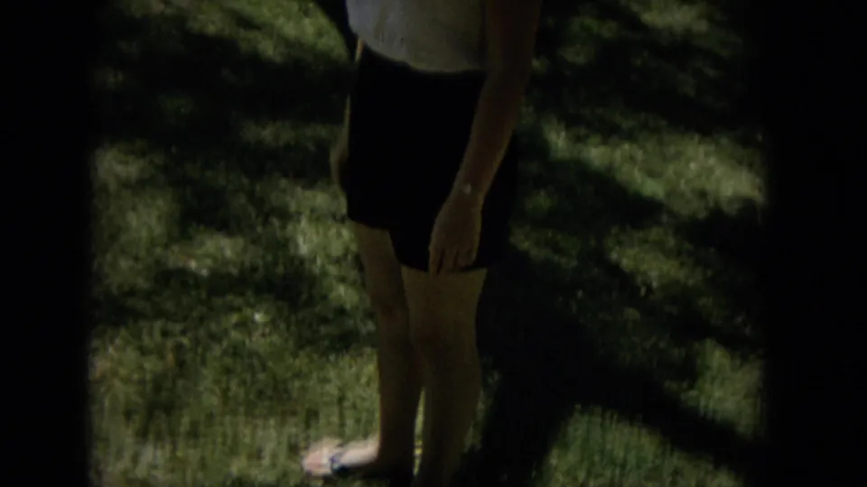 The woman stands in the garden as a dark band obscures part of the contact-sheet frame, leaving her skirt, legs, arm, and shaded lawn clearly visible.