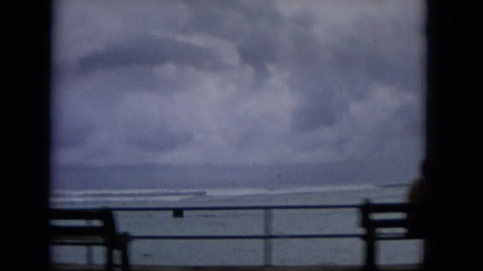 1965 Hawaii coastal promenade view with railings and bench forms silhouetted against a cloudy ocean and sky.