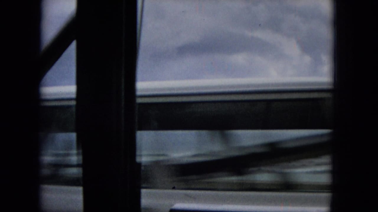 Blurred vehicle roofline and window structure passing against a cloudy coastal view.