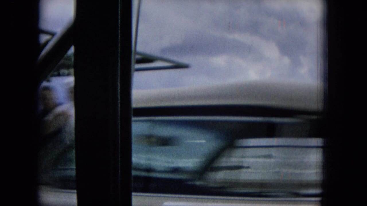 1965 Hawaii 8mm frame showing a blurred car or vehicle side passing close to the camera, framed by dark interior posts with storm clouds beyond.