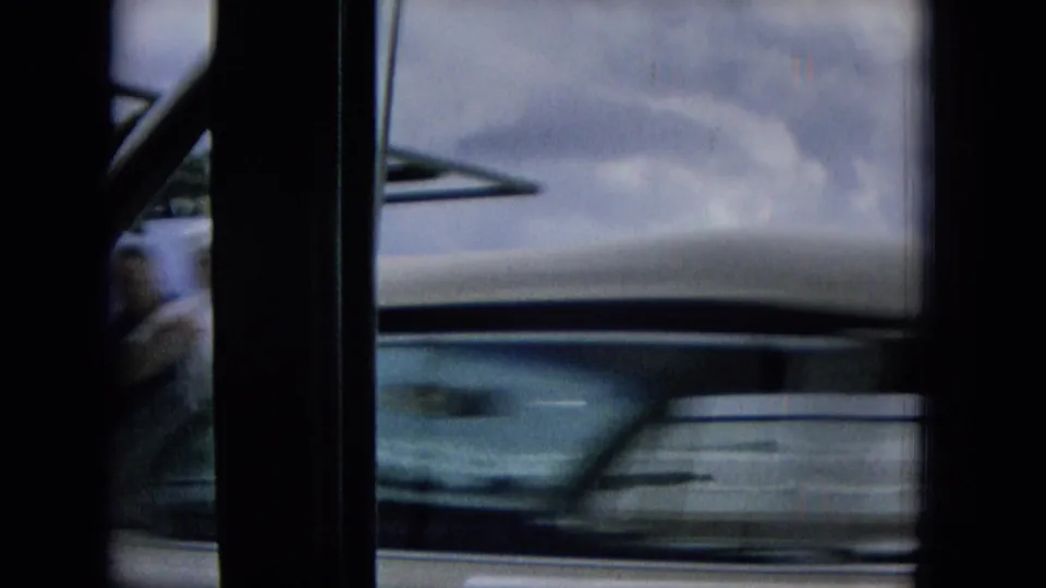 1965 Hawaii 8mm frame showing a blurred car or vehicle side passing close to the camera, framed by dark interior posts with storm clouds beyond.