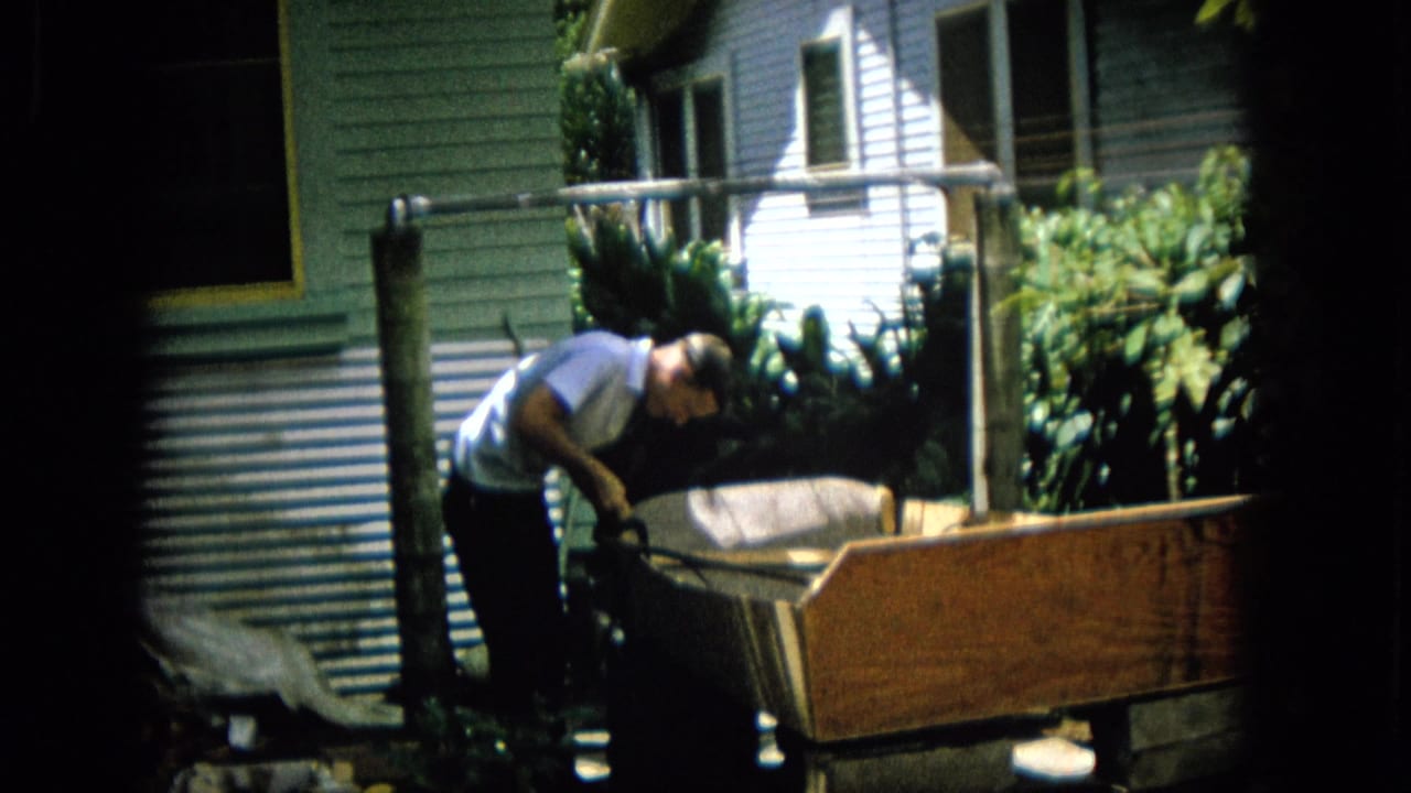 Man leans over a wooden structure near a house exterior.