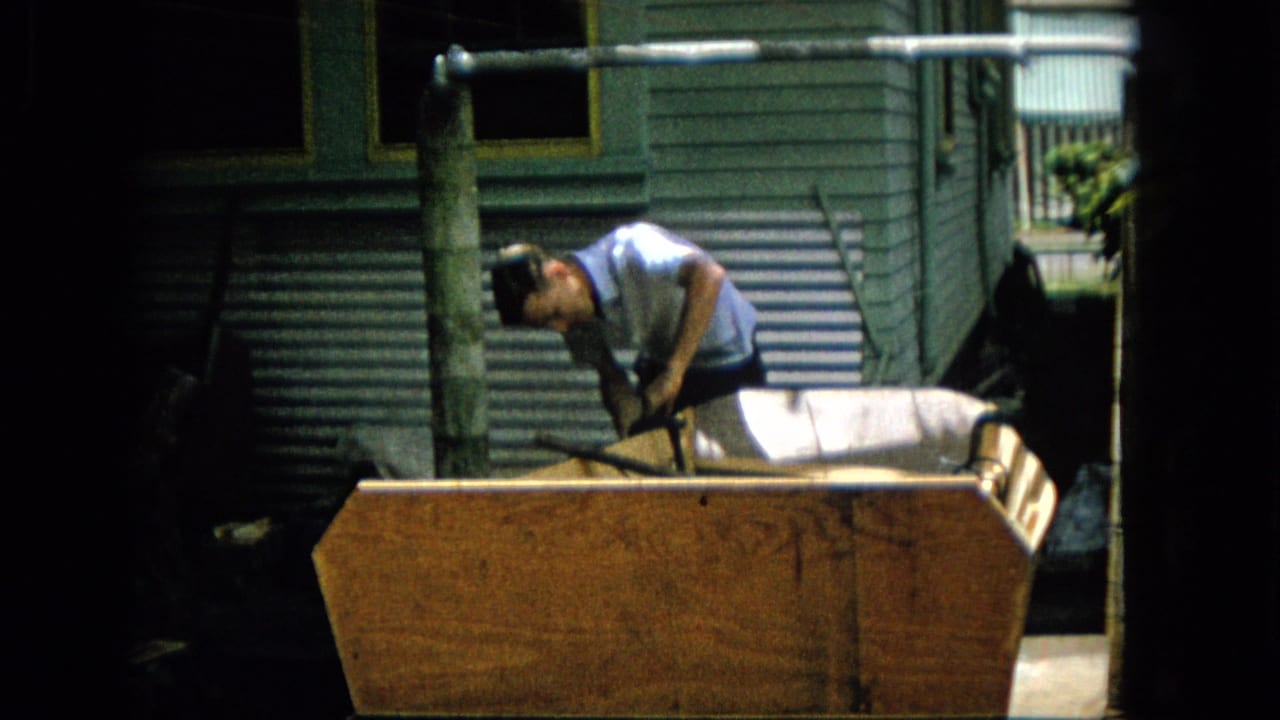 Man bends over a wooden structure while using a tool or handle.