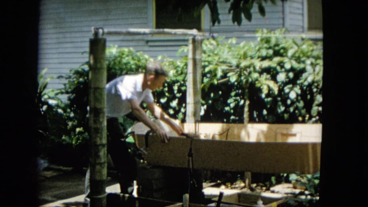 Man leans forward with a tool over the wooden frame in the yard.
