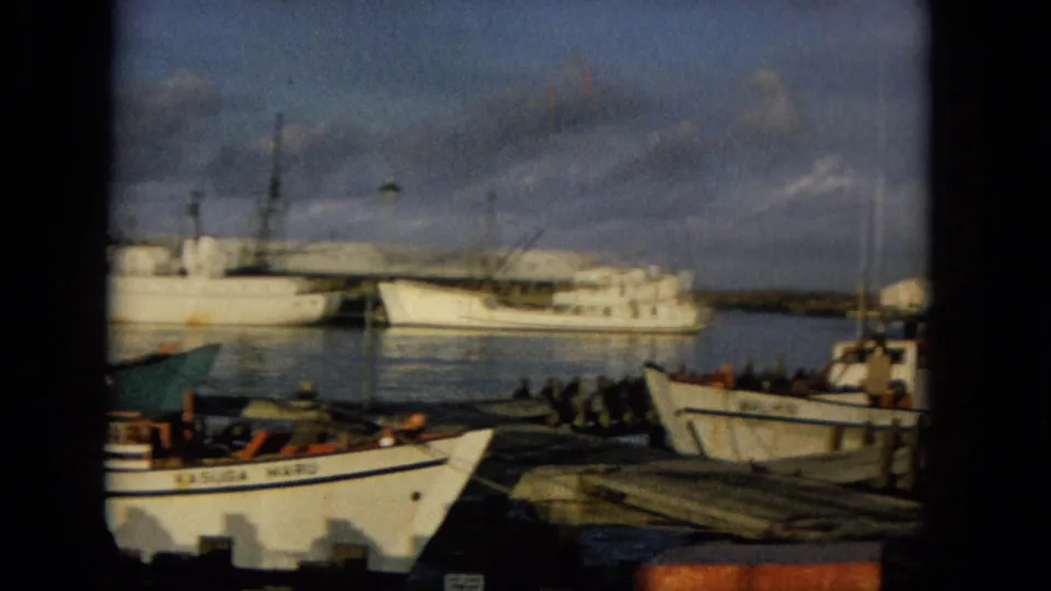 1965 Hawaii home-movie frame of moored harbor boats seen through dark foreground framing, including a vessel marked KASUGA MARU.